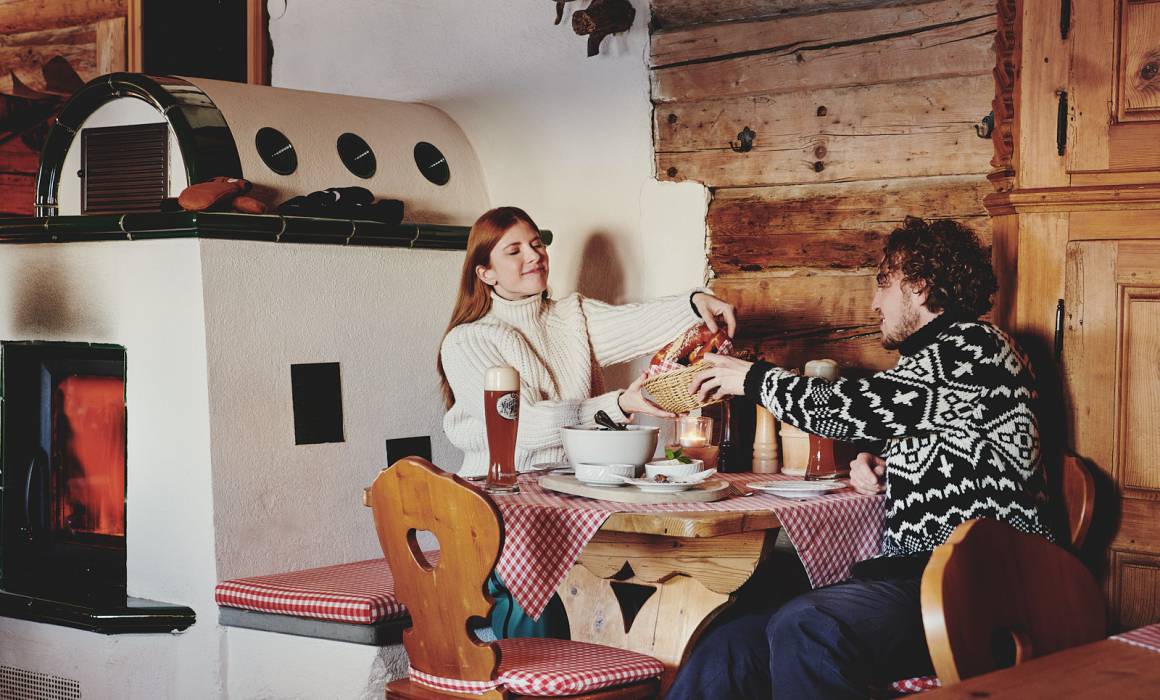 Husband and wife eat in a rustic mountain hut next to the fireplace