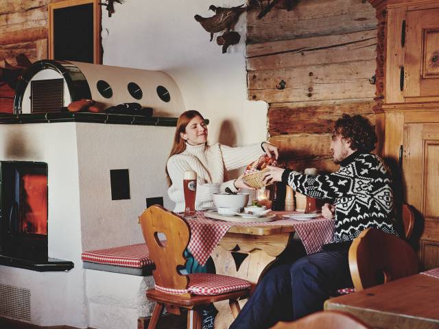 Husband and wife eat in a rustic mountain hut next to the fireplace