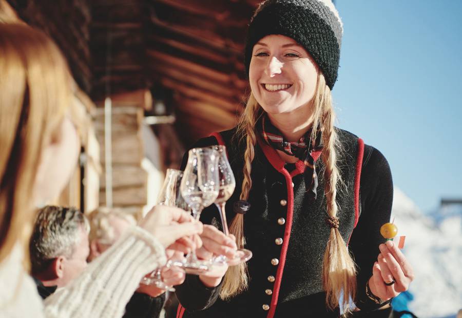 Woman holding pickled mirabelle plums and schnapps in front of a rustic mountain hut